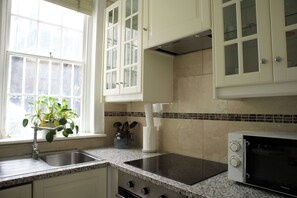 A kitchen with a granite countertop, a built-in stove, a microwave, and white cabinets. - Cozy 3-Bedroom Flat - Fitzrovia & Soho (London)
