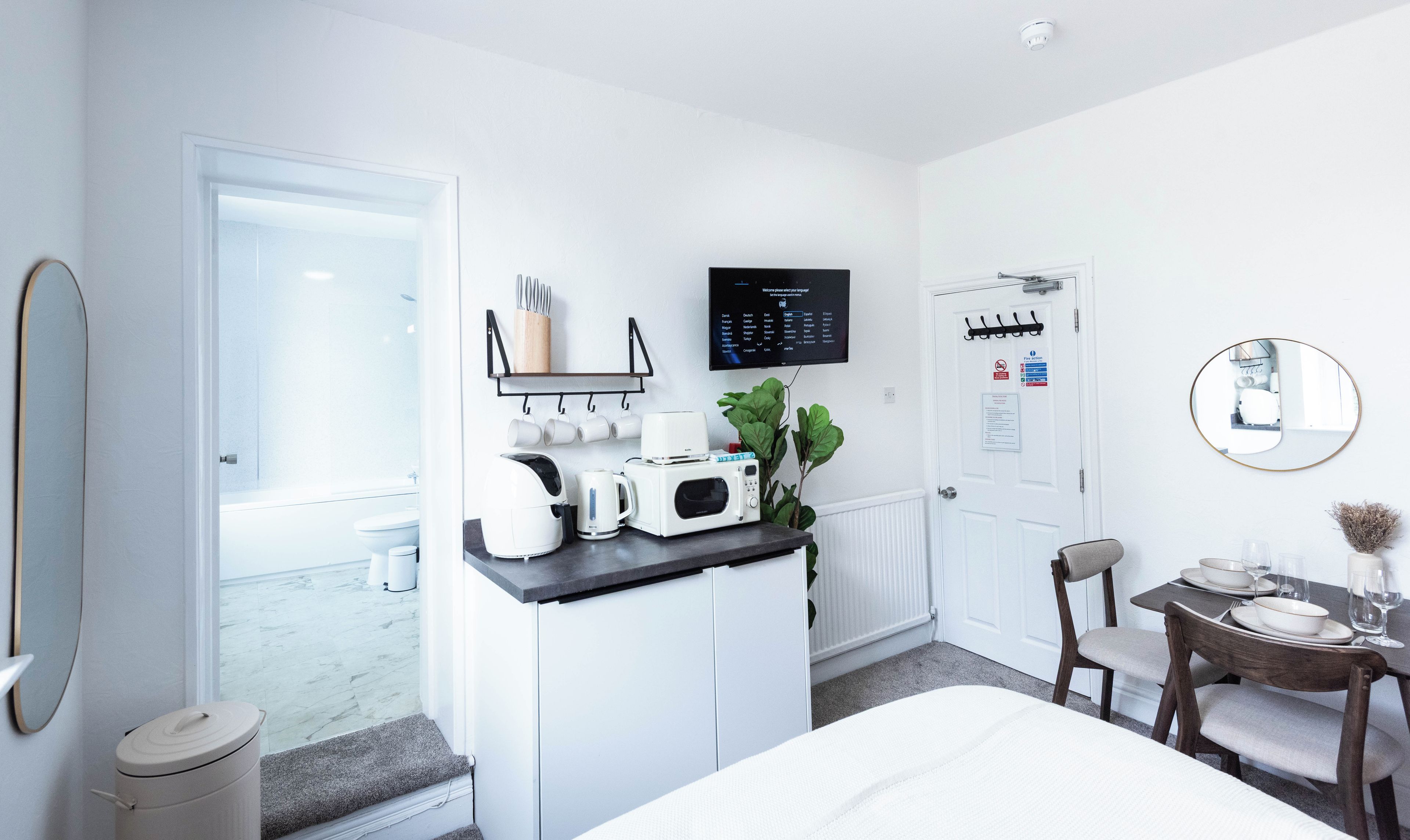 A modern hotel room with a kitchenette, a dining area, and a large mirror.