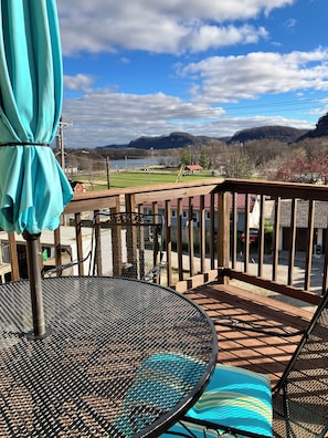 Una terraza con mesa y sillas de metal, con vista a un lago y montañas al fondo.