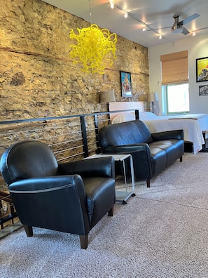 A room with a stone wall, a bed, two black leather chairs, a small table, and a ceiling fan. - Spacious house downtown Lansing with 6 king beds. Can sleep up to 17 guests. (Lansing)
