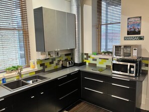 A modern kitchen with black cabinets, a stainless steel microwave, and a toaster. - Spacious home downtown with 6 king beds. Sleeps up to 17 guests, outdoor shower. (Lansing)