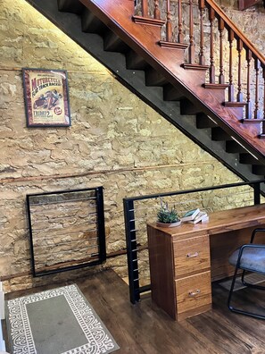 A staircase with wooden balusters, a stone wall, a framed poster, a desk with drawers, and a chair. - Spacious house downtown Lansing with 6 king beds. Can sleep up to 17 guests. (Lansing)