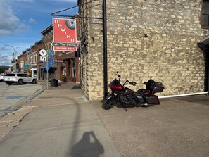 A street with a motorcycle parked by a stone building, a sign for 'UNWIND Biber Retreat', and a 'Stone' sign. - Spacious home downtown with 6 king beds. Sleeps up to 17 guests, outdoor shower. (Lansing)