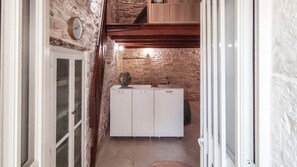 Un pasillo estrecho con pared de piedra, techo de madera y un armario blanco con un jarrón encima.