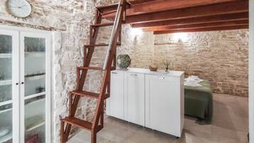 Un intérieur avec un mur en pierre, une échelle en bois, des armoires blanches et une table verte.