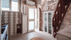 Una habitación con pared de piedra, una puerta blanca, un ventanal y una escalera.