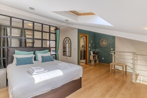 Ein Schlafzimmer mit einem großen Bett, einem Oberlicht, einer Holztreppe und Blick ins Bad.
