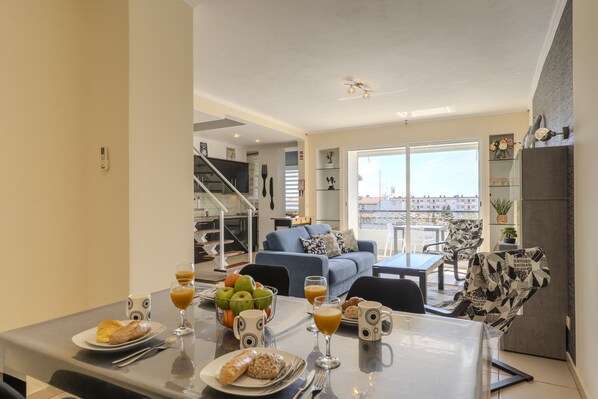 Ein Essbereich mit einem für das Frühstück gedeckten Tisch, einem blauen Sofa und Blick auf die Stadt durch große Fenster.