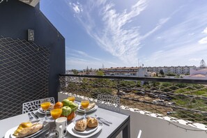 Een balkon met een ontbijtje erop, met uitzicht op een woonwijk met gebouwen en een heldere lucht.