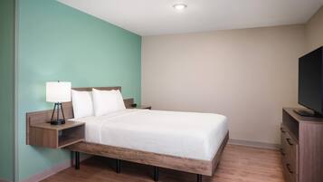 A neatly arranged hotel room with a bed, a nightstand with a lamp, a dresser, and a television.