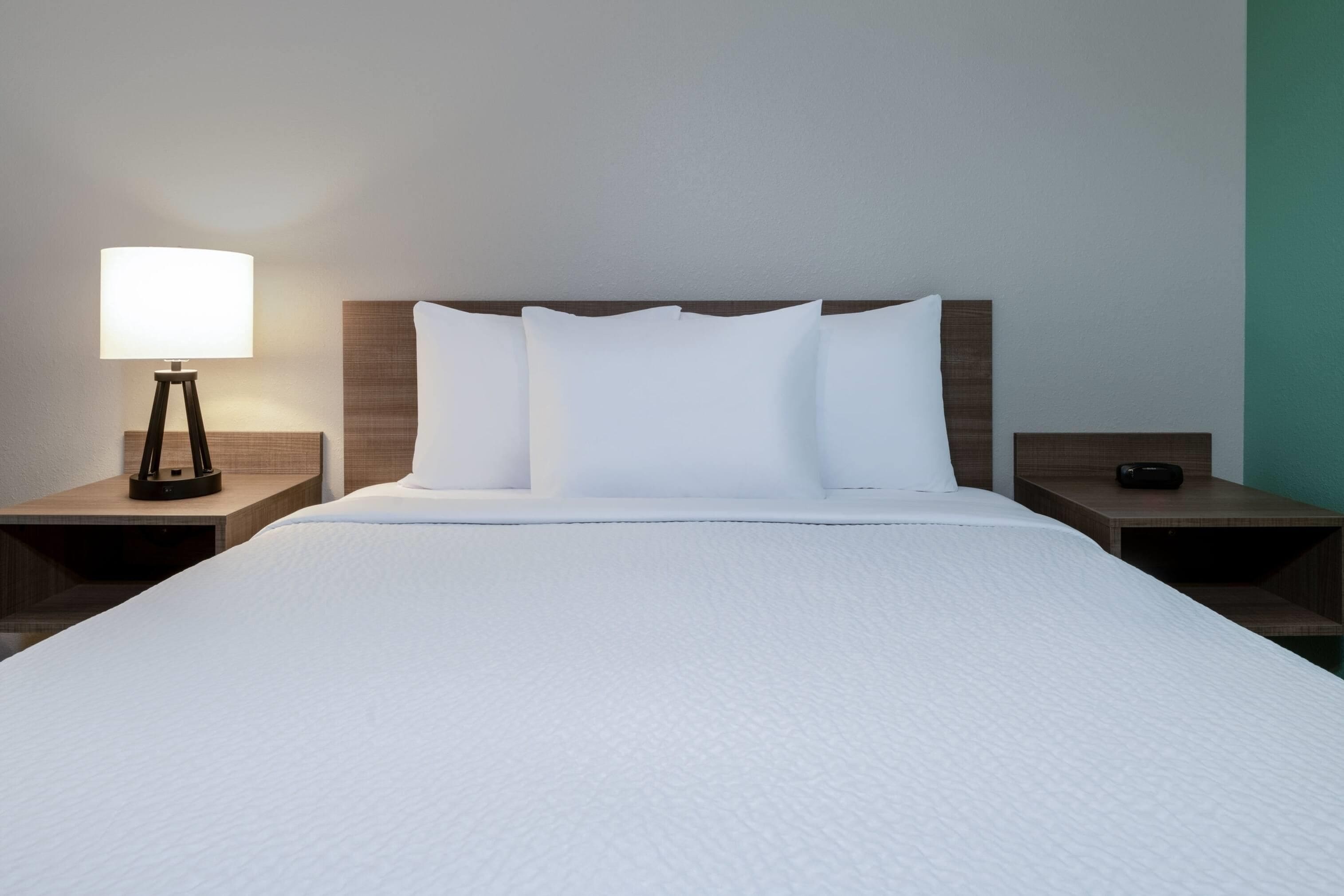 A hotel room with a large bed, white bedding, a bedside lamp, and a nightstand with a remote control.