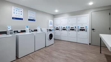 Un cuarto de lavandería con varias lavadoras y secadoras, paneles de control e instructivos carteles en las paredes.