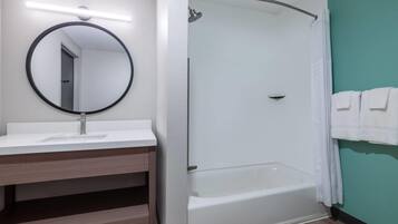 A bathroom with a white bathtub, a round mirror, and a shower area.