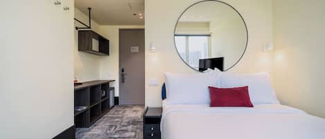 Habitación de hotel con una cama grande, un espejo redondo, una mesita de noche pequeña, un armario y piso alfombrado.