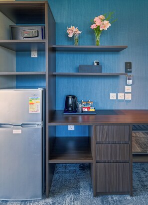 Une petite cuisine équipée d’un réfrigérateur, d’une machine à café et d’un four à micro-ondes. Deux vases avec des fleurs sont posés sur le mur, au-dessus du comptoir.