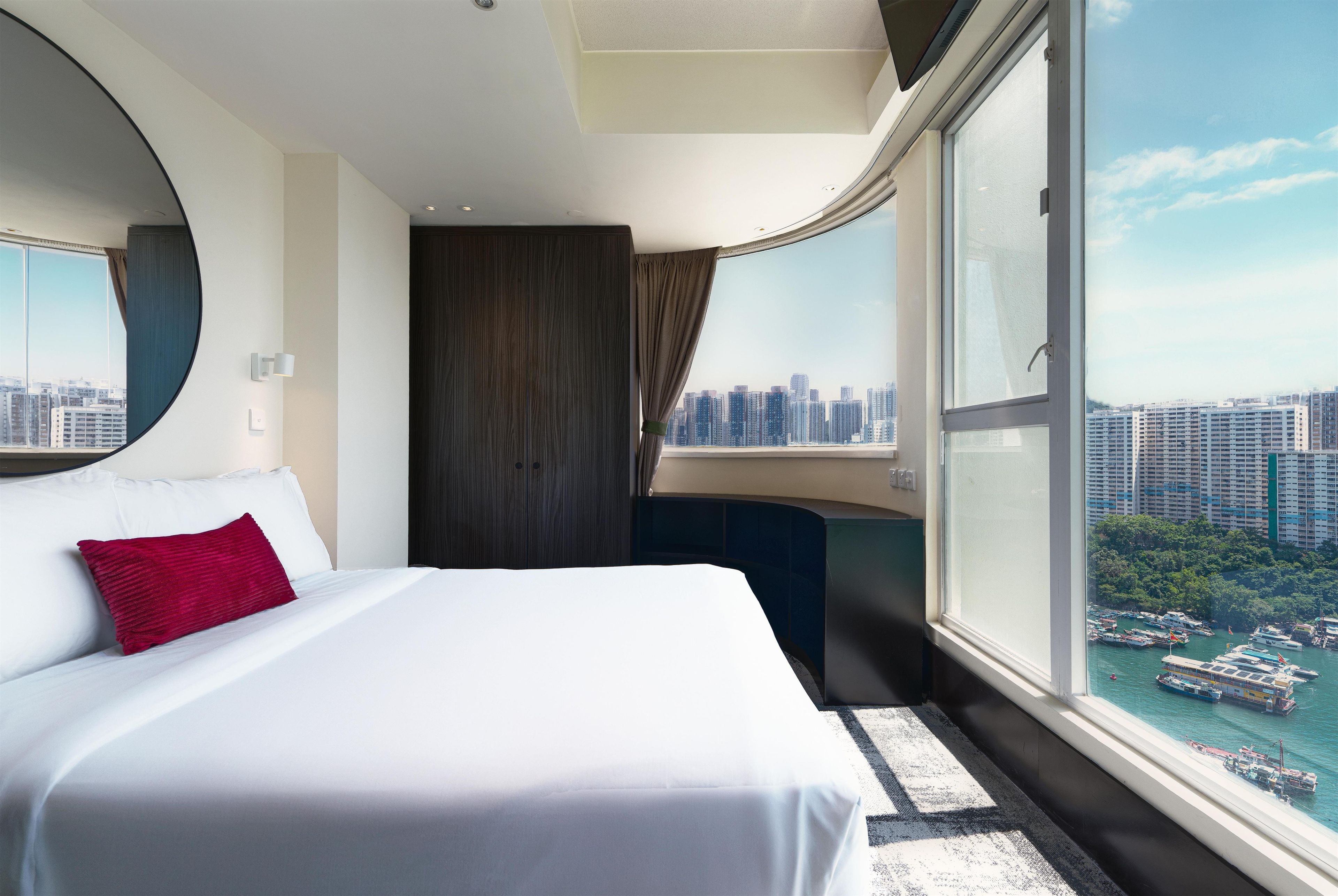 Una habitación de hotel con una cama grande, vistas de la ciudad y una ventana con vista al puerto.