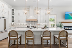 A modern kitchen with white cabinetry, a large island with bar stools, pendant lighting, and a view of the ocean through the window. - Pet Friendly | Bikes | Golf Cart | Private Pool | Spotted Dolphin (Santa Rosa Beach)