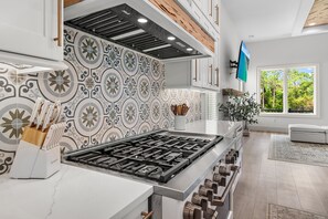 Une cuisine moderne dotée d’un îlot central, d’un crédence décorée et d’une fenêtre donnant sur un paysage verdoyant.