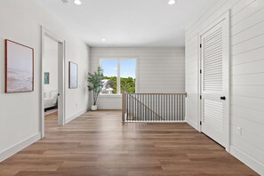 Un couloir doté d’un plancher en bois, de murs blancs et offrant une vue sur l’extérieur grâce à une grande fenêtre.