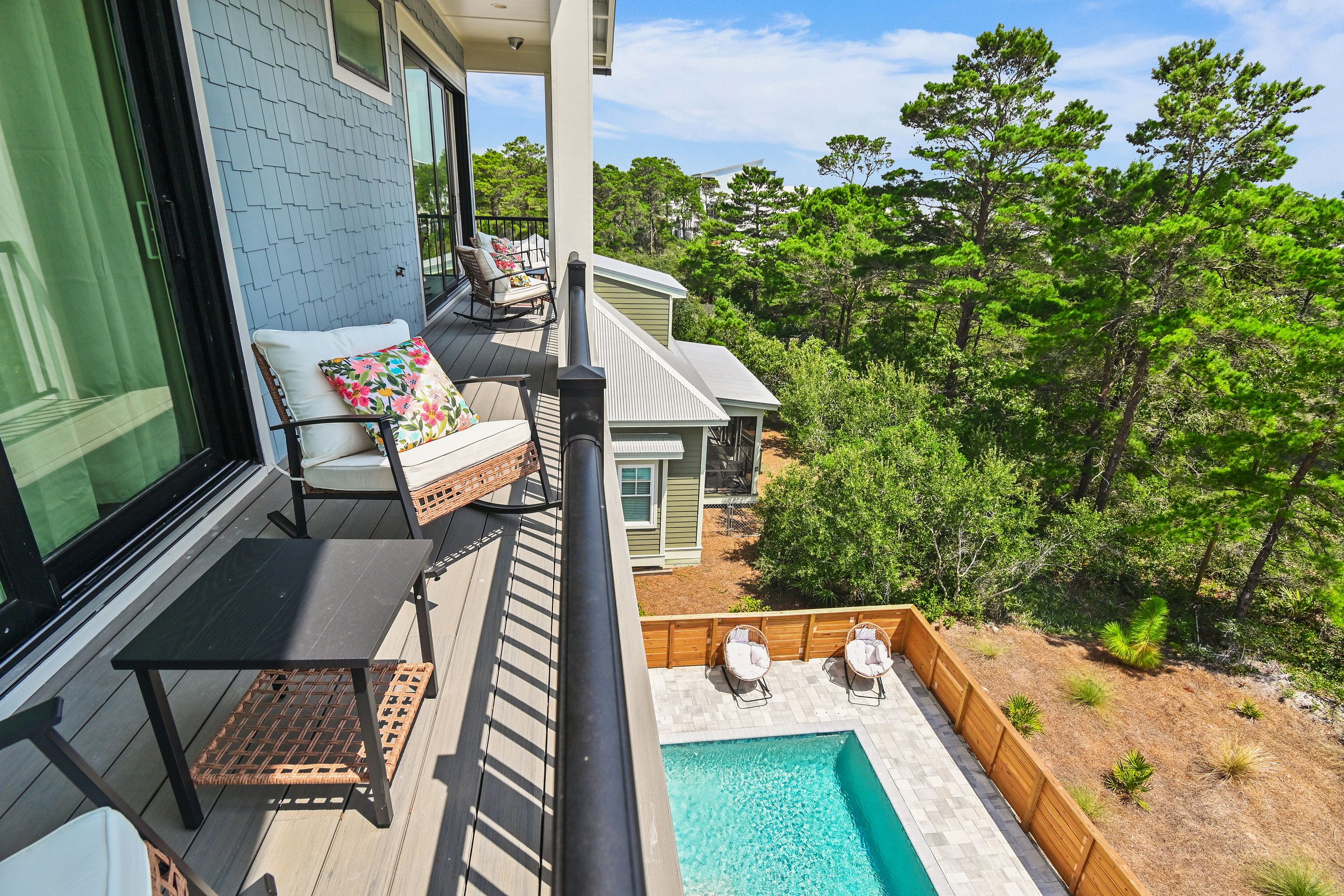 A balcony with outdoor furniture, a pool, and a view of the surrounding greenery.