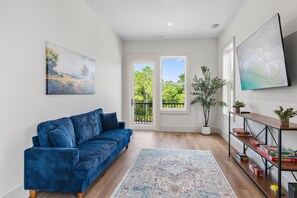 A living room with a blue sofa, a large painting, a potted plant, and a game shelf. - Pet Friendly | Bikes | Golf Cart | Private Pool | Spotted Dolphin (Santa Rosa Beach)