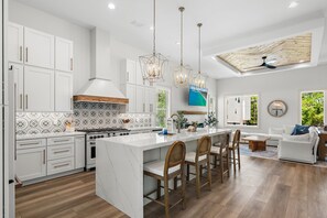 A modern kitchen with white cabinetry, a large island, and a dining area with wooden chairs. - Pet Friendly | Bikes | Golf Cart | Private Pool | Spotted Dolphin (Santa Rosa Beach)