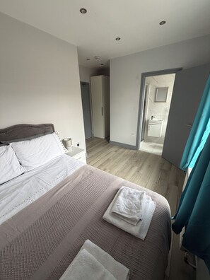 Ein Schlafzimmer mit Bett, Schrank, Badezimmer mit Spiegel und einer Tür zu einem anderen Raum.