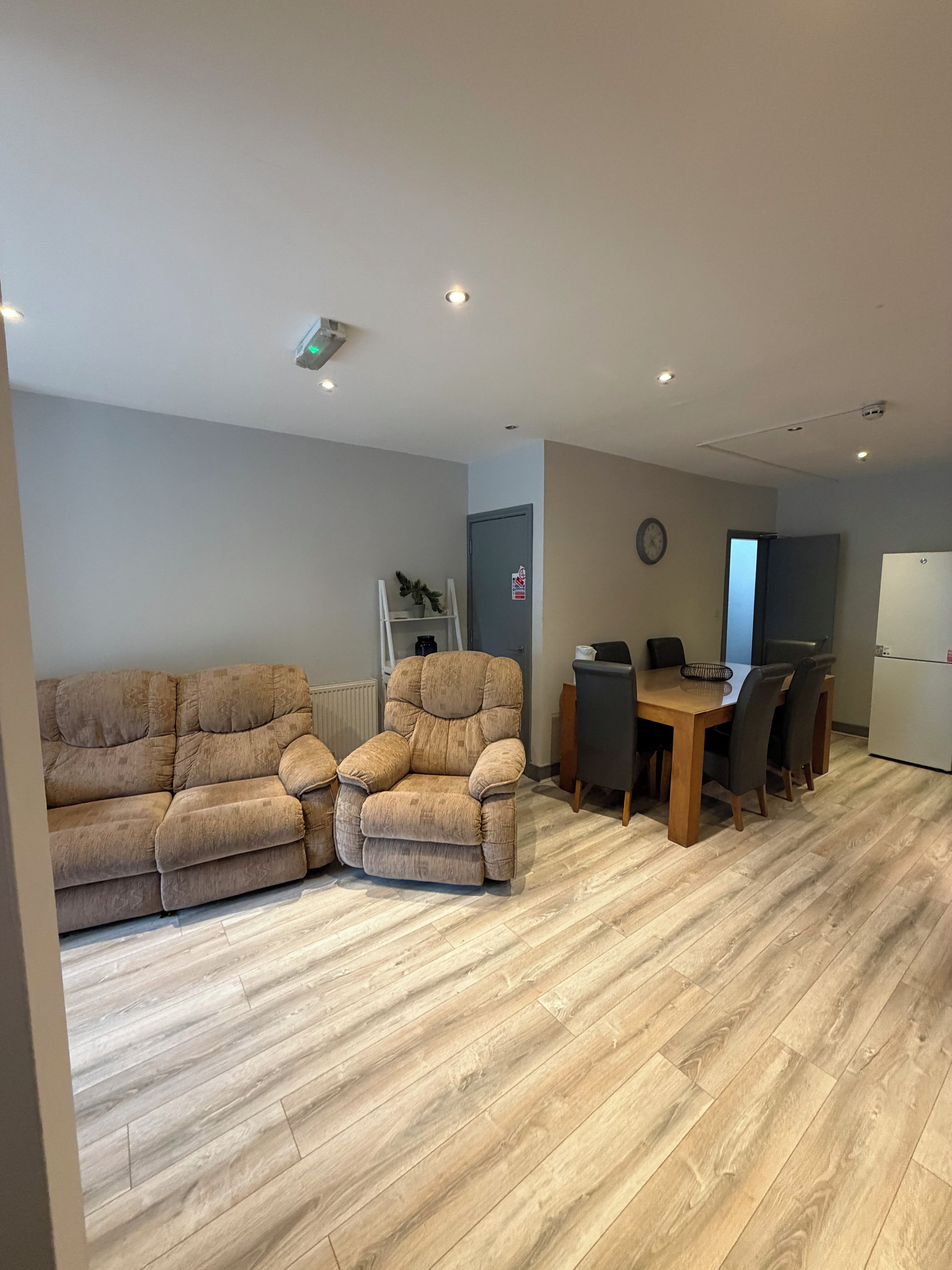 Ein Wohnzimmer mit einer Couch, einem Esstisch mit Stühlen und einer Küchenzeile inklusive Kühlschrank.