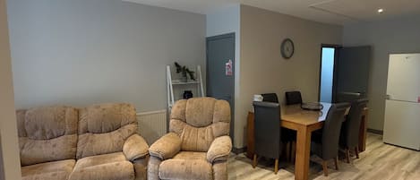 Ein Wohnzimmer mit einer Couch, einem Esstisch mit Stühlen und einer Küchenzeile inklusive Kühlschrank.