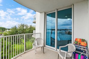 A balcony with a white railing, two white plastic chairs, and a colorful bag on the floor. - 🌴Beach Nearby + Lagoon Pool | Fab Amenities | Palms Resort 1404☀️ (Destin)