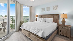 A hotel room with a large bed, two bedside tables with lamps, a ceiling fan, and a view of the city through the balcony. - 🌴Beach Nearby + Lagoon Pool | Fab Amenities | Palms Resort 1404☀️ (Destin)