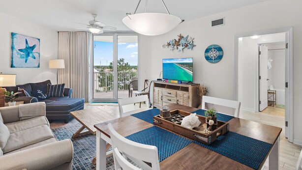 A modern living room with a dining area, a large window with a view, and a ceiling fan. - 🌴Beach Nearby + Lagoon Pool | Fab Amenities | Palms Resort 1404☀️ (Destin)