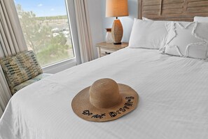 Ein Hotelzimmer mit Bett, Lampe, Fenster mit Aussicht und einem Hut auf dem Bett.