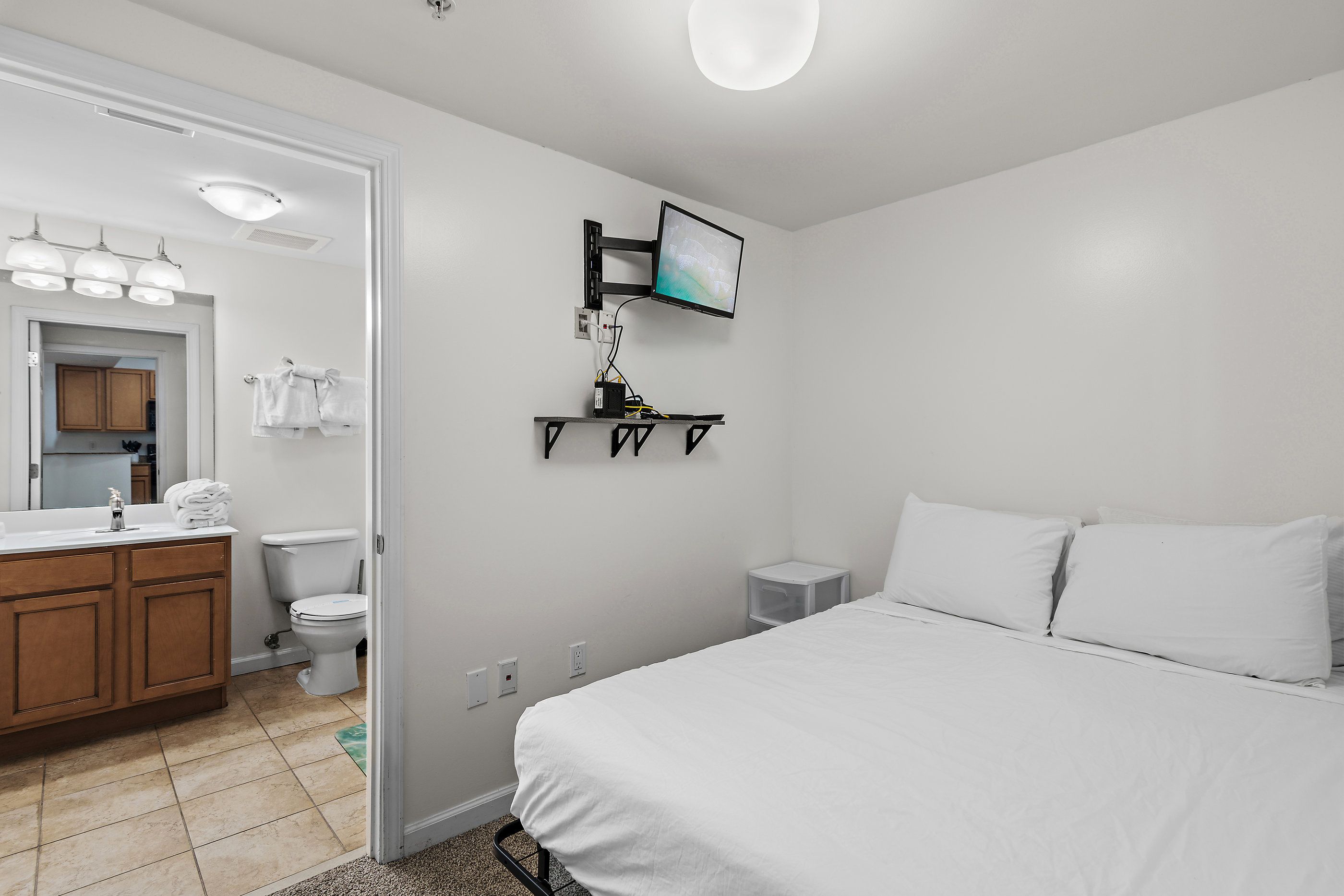 Une chambre d’hôtel comprenant un lit, une table de chevet, un téléviseur fixé au mur et une salle de bain avec des toilettes, un lavabo et un porte-serviettes.