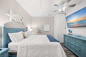Ein Schlafzimmer mit einem Bett, einem Deckenventilator, einem an der Wand montierten Fernseher und einer Kommode.
