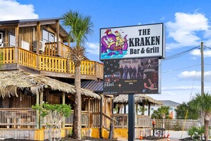 Ein Holzgebäude mit einem Schild für 'The Kraken Bar & Grill', das eine Illustration eines Piratenschiffs zeigt.