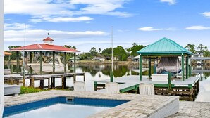 A tranquil pool area with a gazebo, a boat dock, and a calm lake. - 🎣Angler Dock House | Private Pool | Lagoon View | Close to Beach🌊 (Panama City Beach)