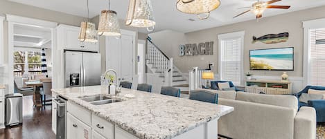 A spacious kitchen with a large island, white cabinetry, and a stainless steel refrigerator.