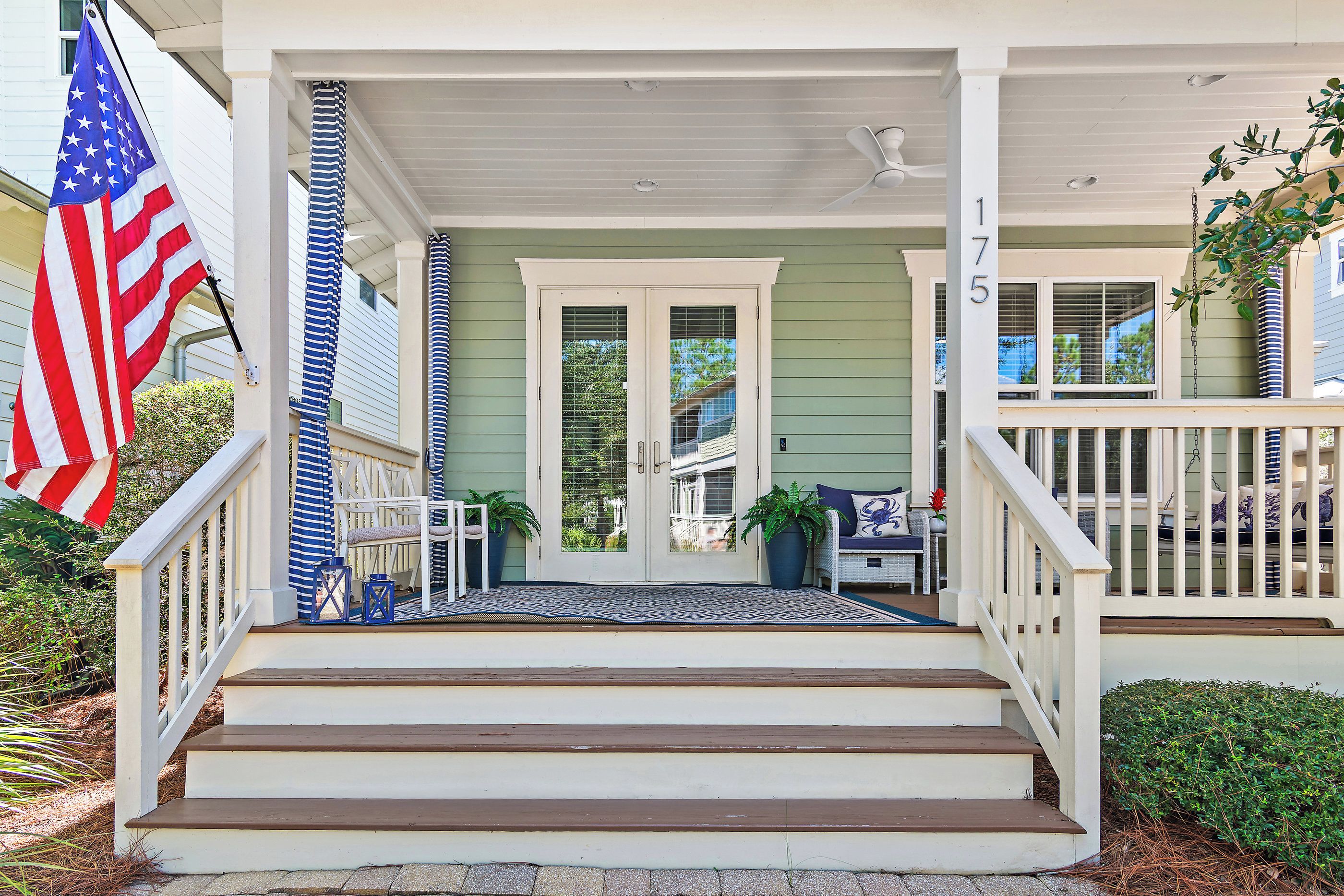 A front porch with a set of wooden steps leading to a door, a flag, and a mailbox.