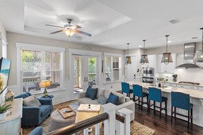 A modern kitchen with a central island, bar seating, and a ceiling fan. - 🌴Sea Esta | 4BR Coastal Retreat | Golf Cart + 6 Bikes | NatureWalk🌴 (Santa Rosa Beach)
