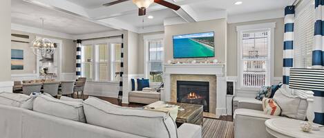 A spacious living room with a fireplace, a ceiling fan, and a television mounted above it.