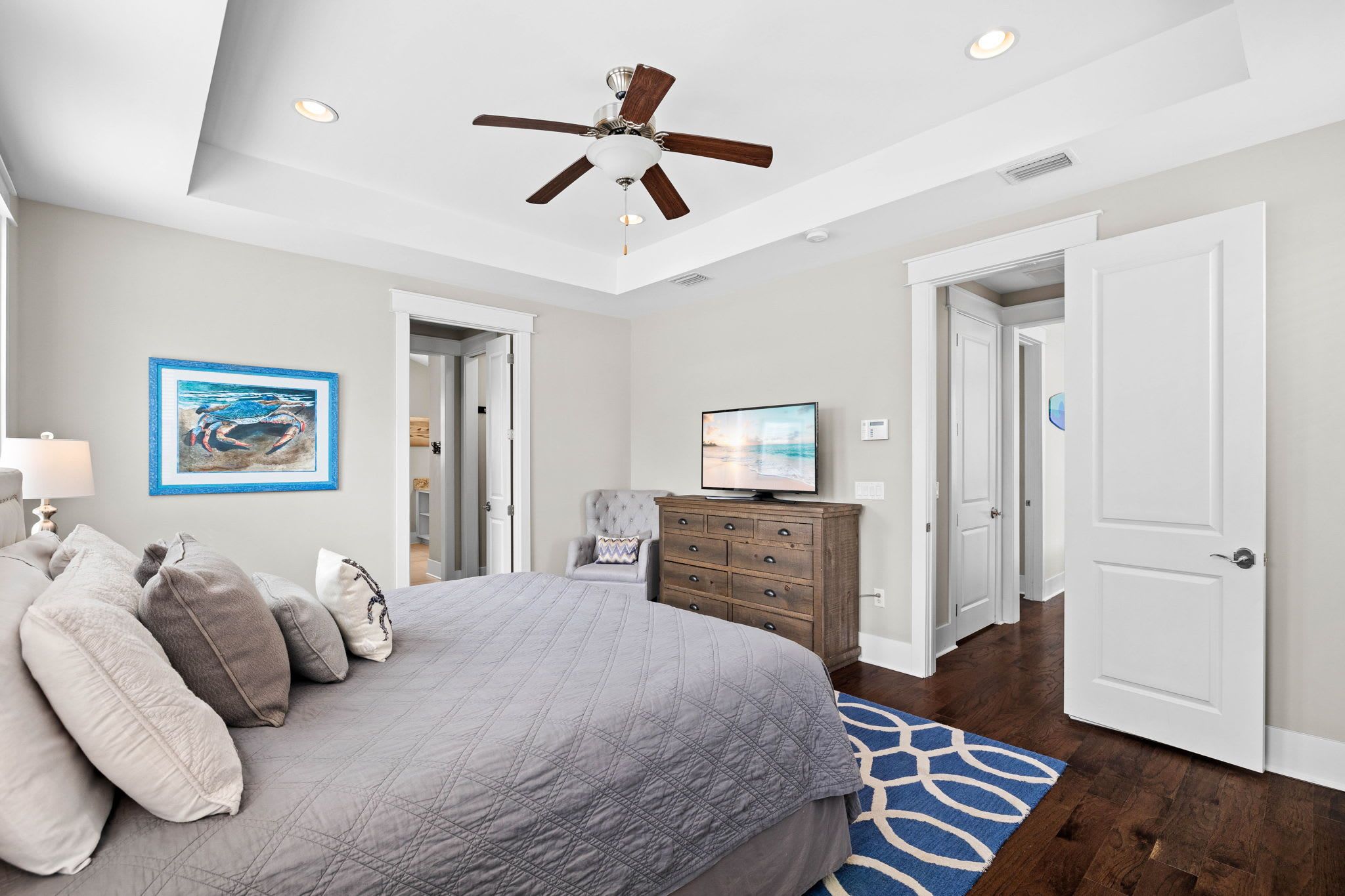 A bedroom with a bed, a ceiling fan, a television, a dresser, and a door.