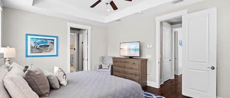 A bedroom with a bed, a ceiling fan, a television, a dresser, and a door.