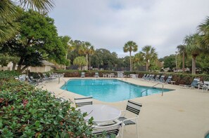 Ein Swimmingpool mit Liegestühlen und Tischen, umgeben von Palmen und viel Grün.