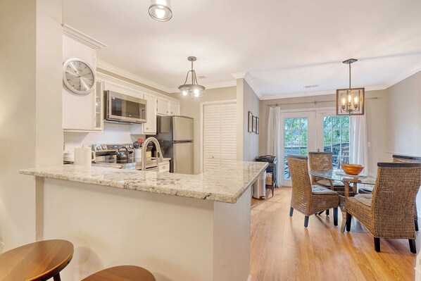 A kitchen with a marble countertop, stainless steel appliances, and a dining area with wicker chairs and a glass table. - 2bed/1.5bath duplex; central Mount Pleasant, Near Beaches + Downtown! (Mount Pleasant)