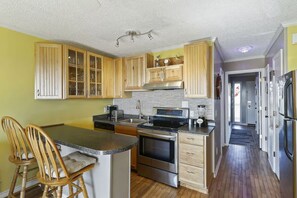 A kitchen with wooden cabinets, stainless steel appliances, and a central island with seating. - Front beach condo with amazing view, pool access, beach access, and pier! (Isle of Palms)