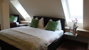 Une chambre avec un grand lit, deux tables de chevet, une fenêtre et un puits de lumière.