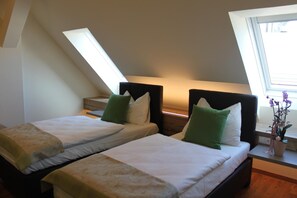 A room with two beds, each with a headboard and pillows, a small table with a vase of flowers, and a window with a view. - Hotel Braun (Voitsberg)