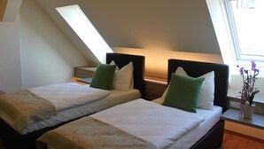 Une chambre avec deux lits, chacun doté d’une tête de lit et d’oreillers, une petite table sur laquelle est posé un vase de fleurs, et une fenêtre offrant une vue agréable.