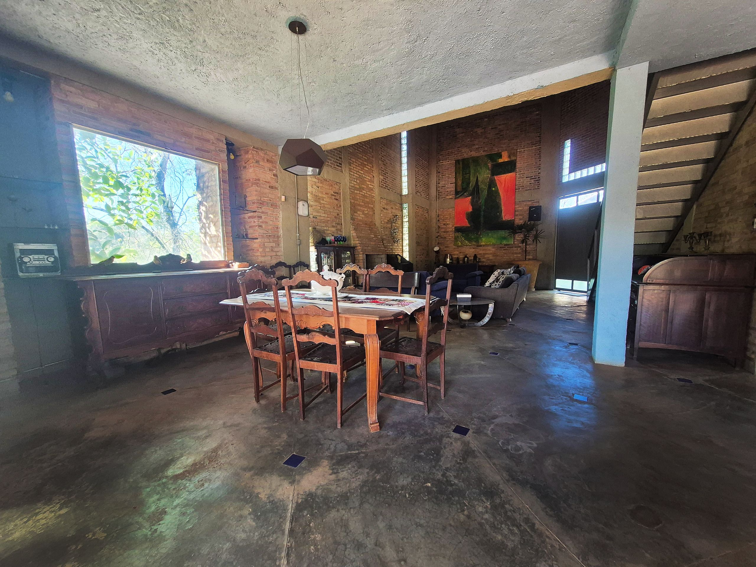 A rustic interior with exposed brick walls, a dining area with wooden chairs and a table, and a staircase leading to an upper level.